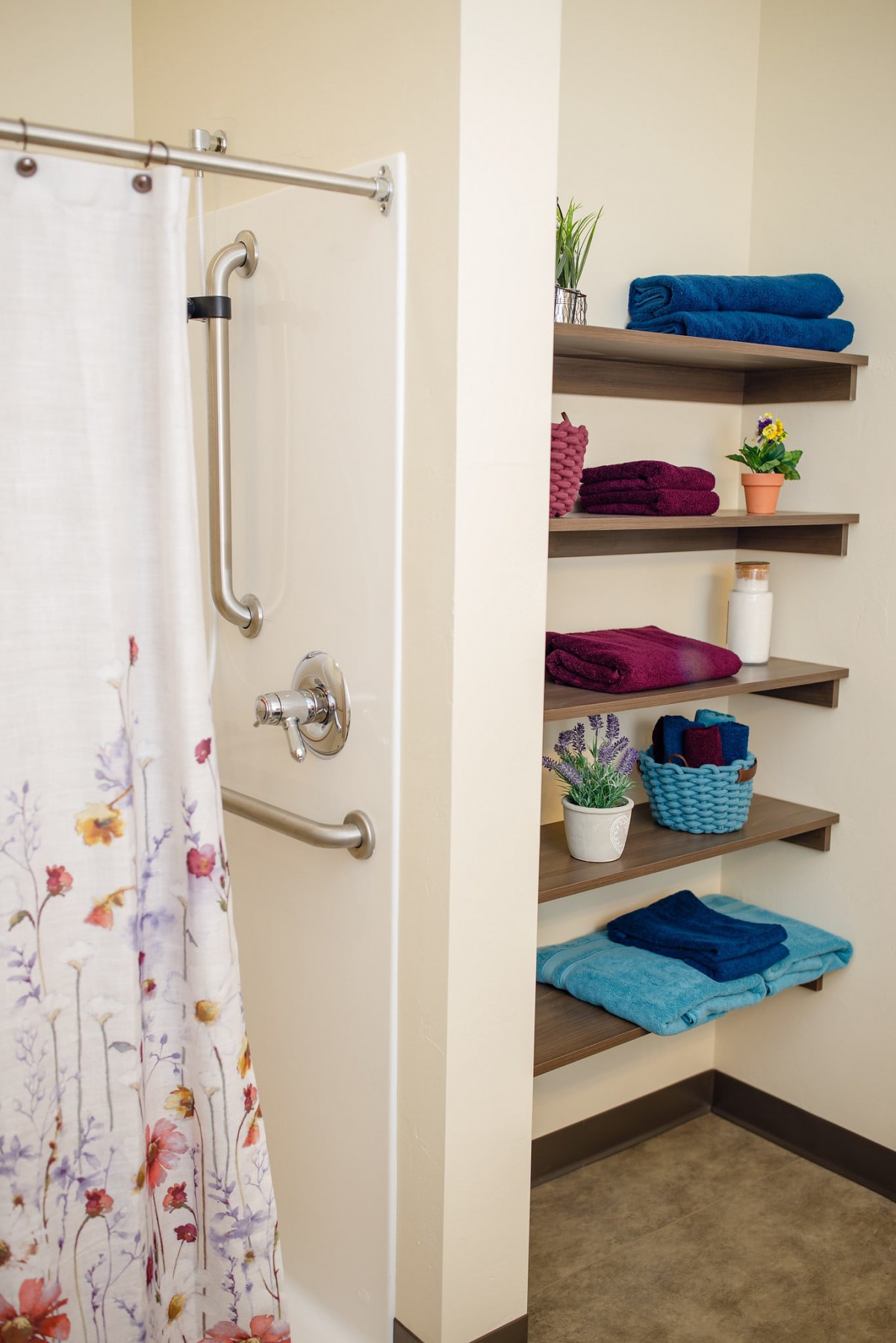 A neatly organized bathroom with colorful towels on shelves and a shower area.