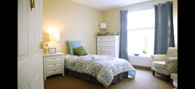 A cozy bedroom with a single bed, dresser, and natural light from a large window.