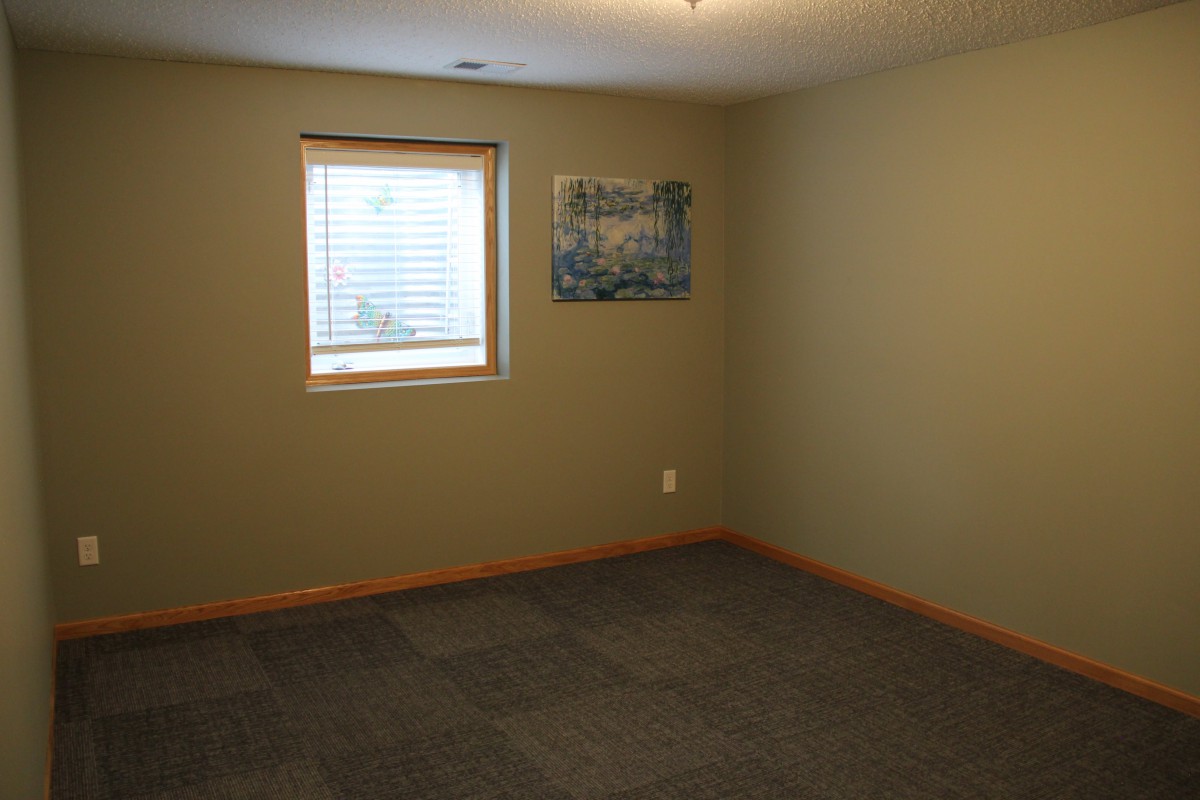 An empty room with beige walls, a window, and a piece of wall art.