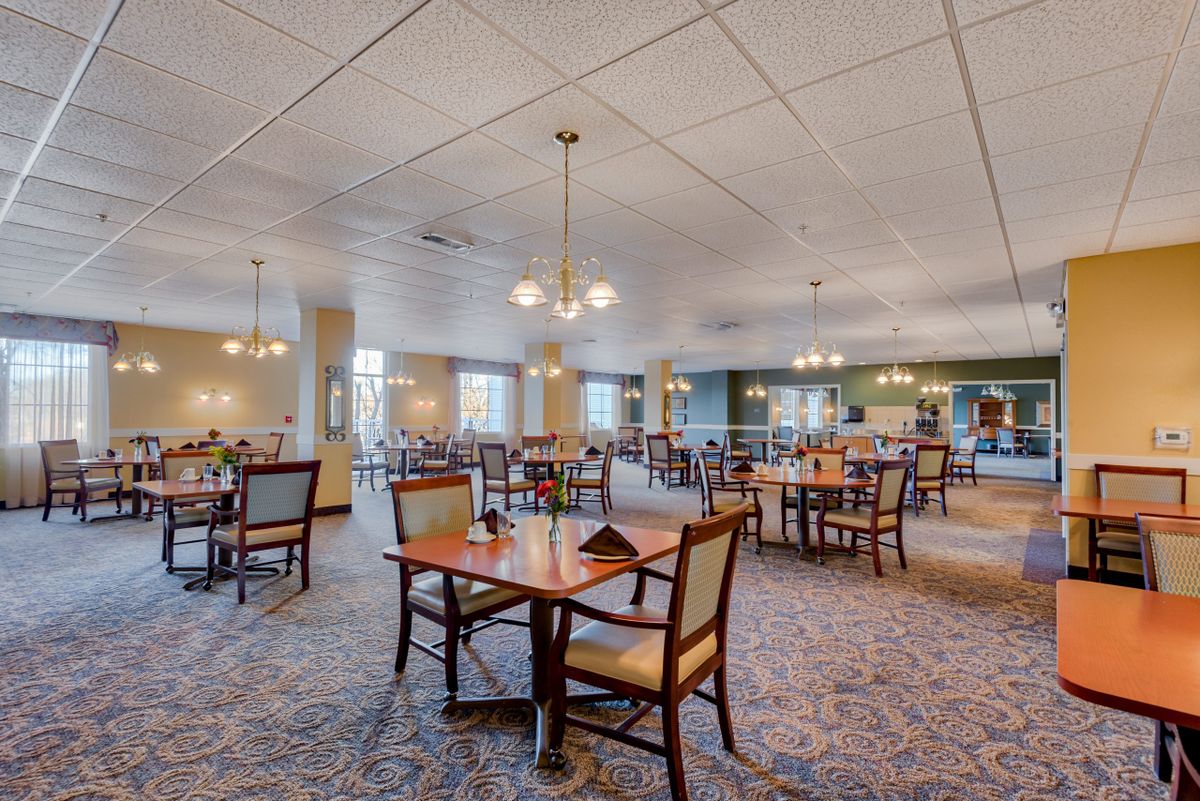 A spacious dining room with neatly arranged tables and chairs, featuring elegant lighting.