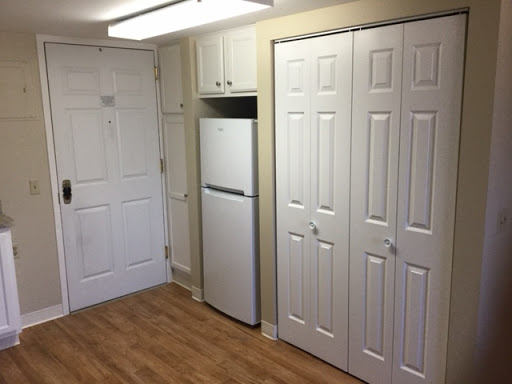 A small kitchen area featuring a refrigerator and storage closets with a warm wooden floor.