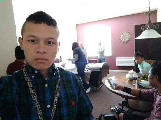 A selfie taken indoors, showing a person in a plaid shirt with others in the background.
