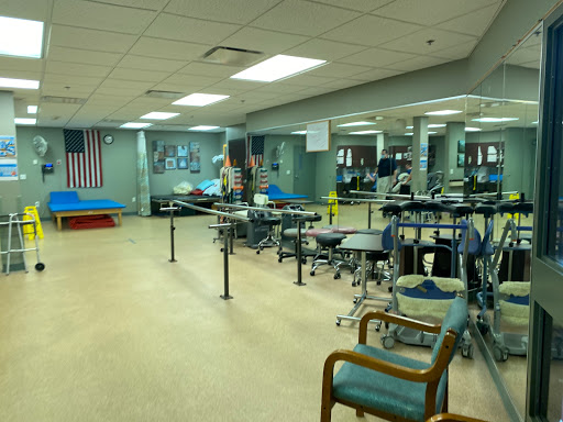 An interior view of a rehabilitation center featuring exercise equipment, chairs, and mirrors.