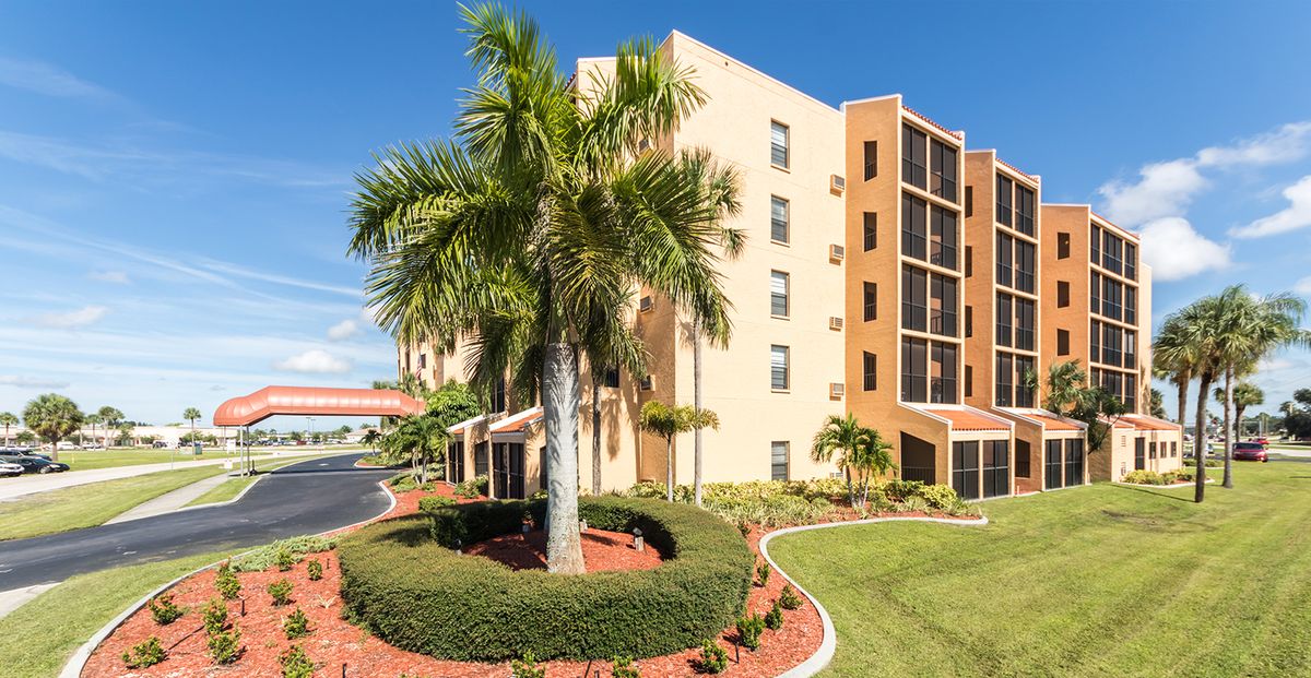 A sunny day view of an apartment building with a palm tree and landscaped garden.