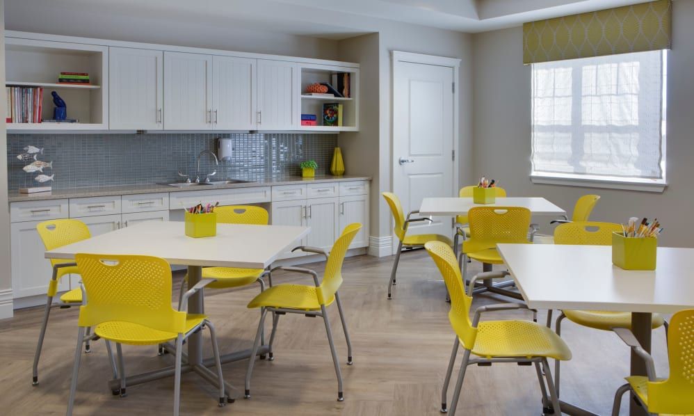 A modern kitchen dining area featuring yellow chairs and white cabinets with a wooden floor.