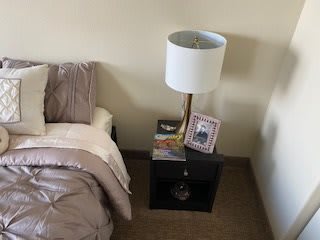 A neatly arranged bedroom nightstand with a lamp, picture frame, and books beside a bed.