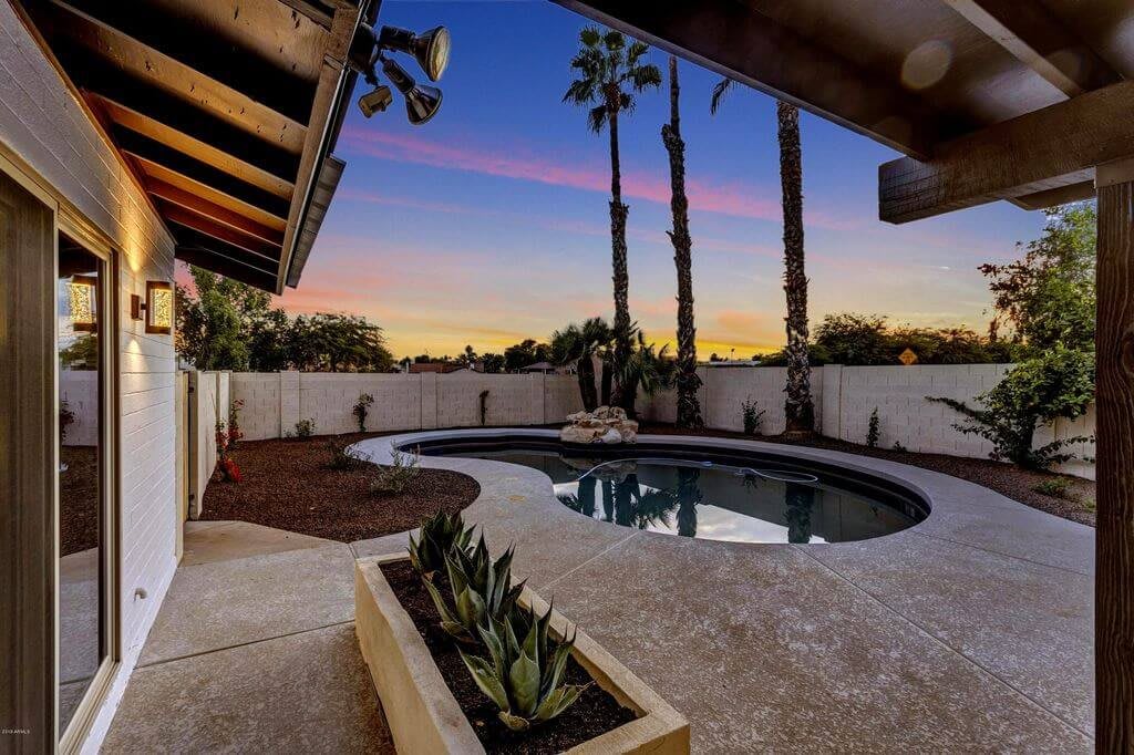 A serene backyard with a swimming pool, surrounded by palm trees at sunset.