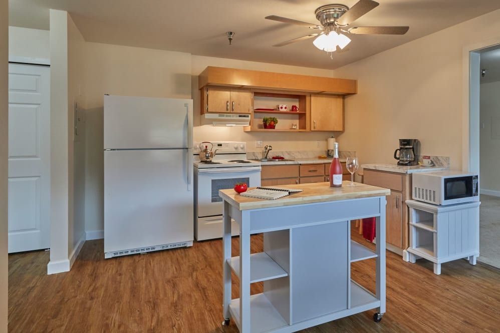 A modern kitchen with wooden flooring, featuring a refrigerator, stove, and a central island.