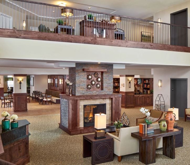 A modern lobby area featuring stylish furniture and a central fireplace, with an open mezzanine above.