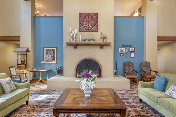A cozy living room featuring a stylish fireplace, wooden coffee table with a flower vase, surrounded by blue walls and decorative artwork.
