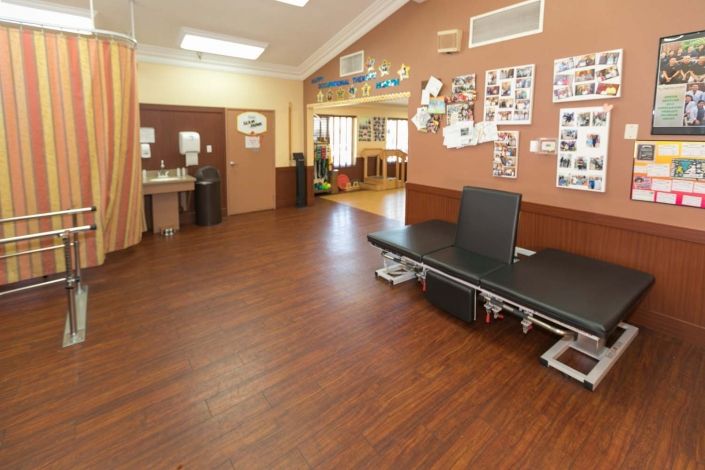 A spacious rehabilitation room in a clinic, equipped with treatment tables and exercise equipment.