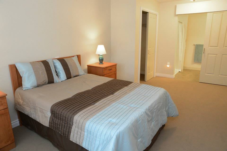 A cozy bedroom with a neatly made bed, bedside lamp, and simple decor.