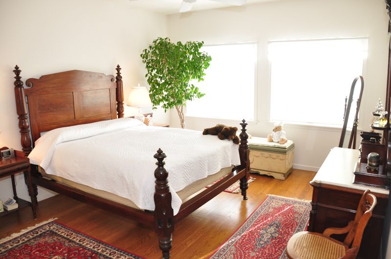 A bright bedroom with wooden furniture and a large bed, featuring natural lighting and indoor plants.