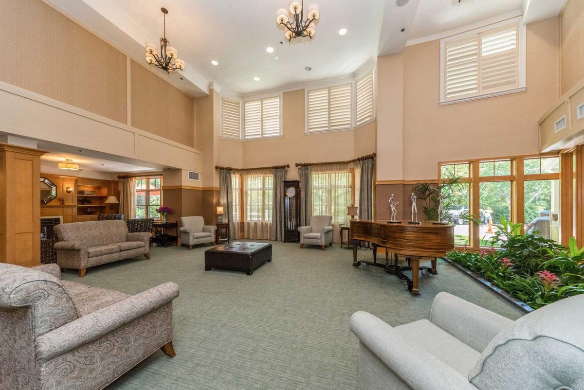 A spacious and elegantly furnished lobby featuring multiple sofas, a grand piano, large windows, and chandeliers.