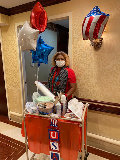 A vendor decorated with balloons stands beside her snack trolley, ready to celebrate.