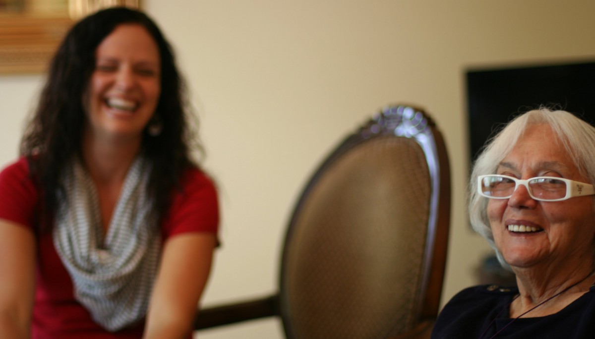 A woman smiling indoors with a chair in the foreground.