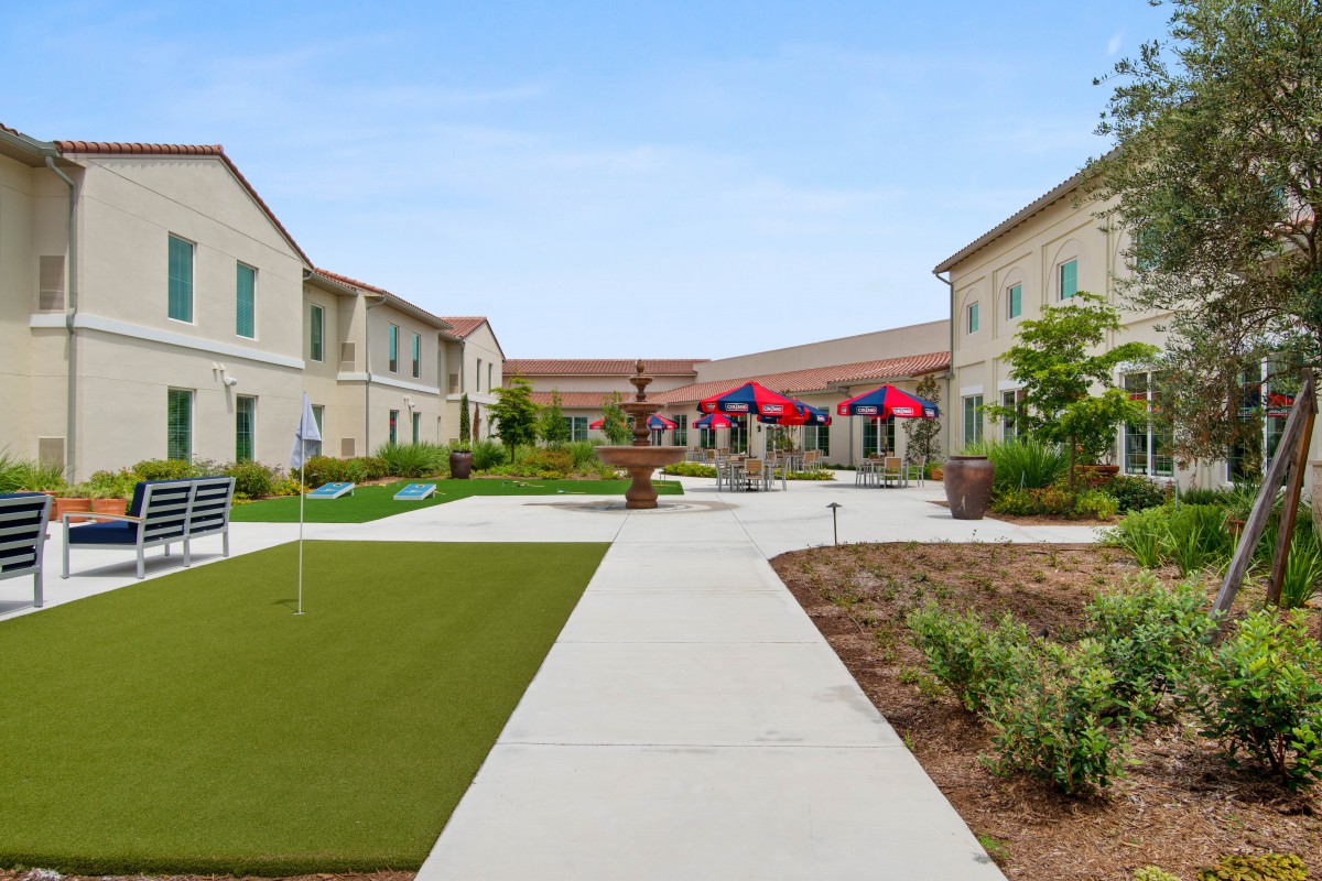 A courtyard with a walkway surrounded by buildings, featuring landscaping and flags.