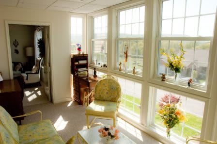 A sunny living room with large windows, floral decor, and cozy seating.