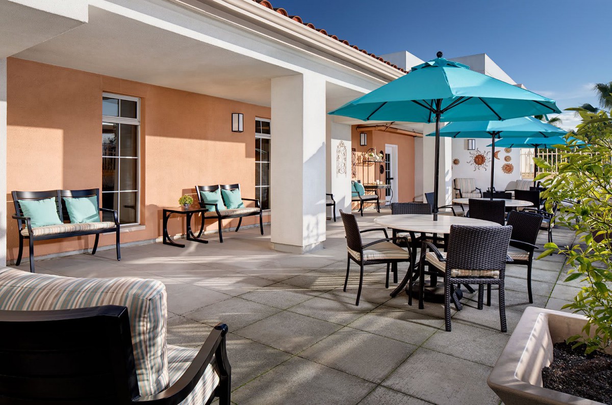 A sunny outdoor patio area with tables, chairs, and umbrellas.