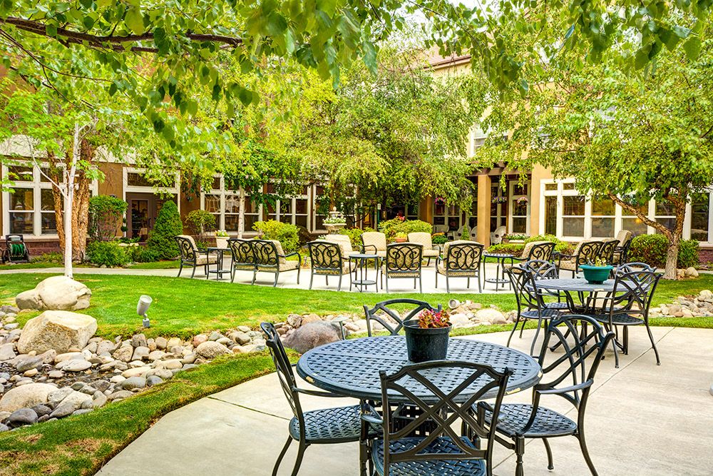 A peaceful garden patio with tables and chairs surrounded by lush greenery.