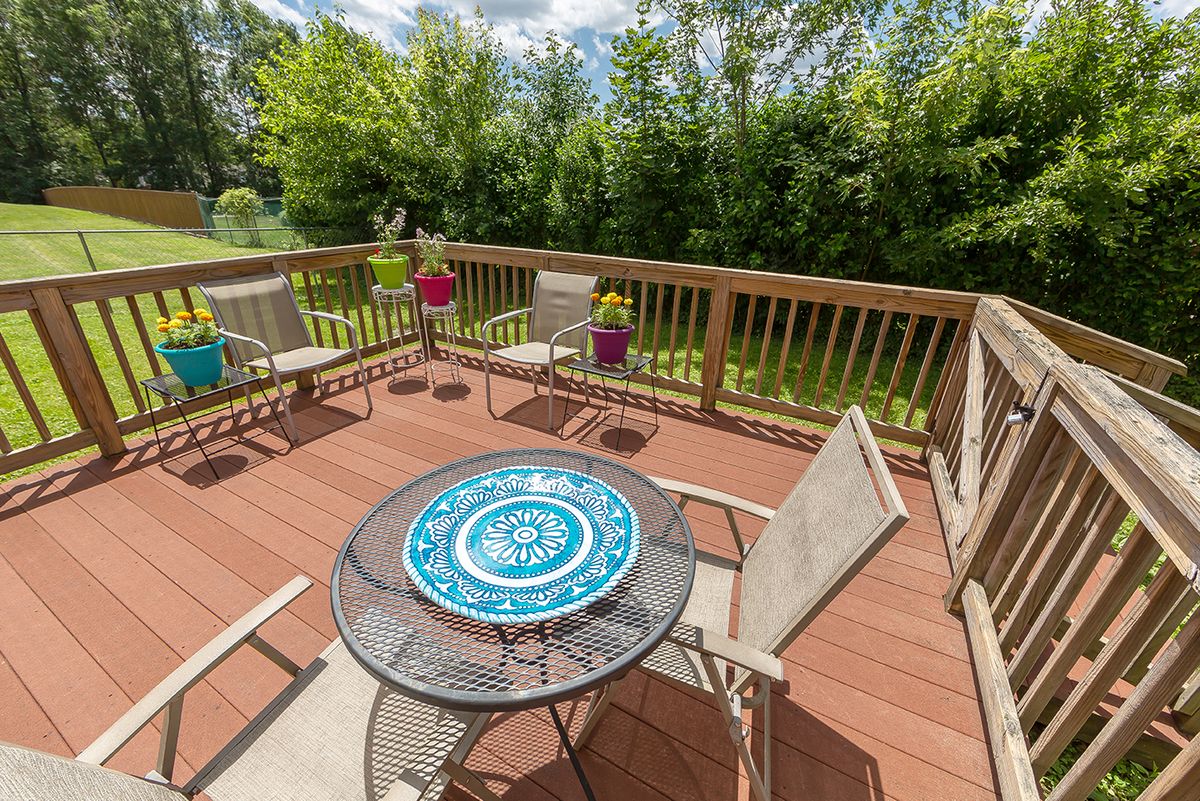 A sunny wooden deck with patio furniture and vibrant greenery in the background.