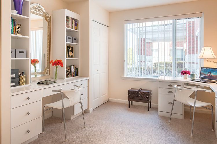A bright, well-organized bedroom with a vanity table and mirror near a large window.