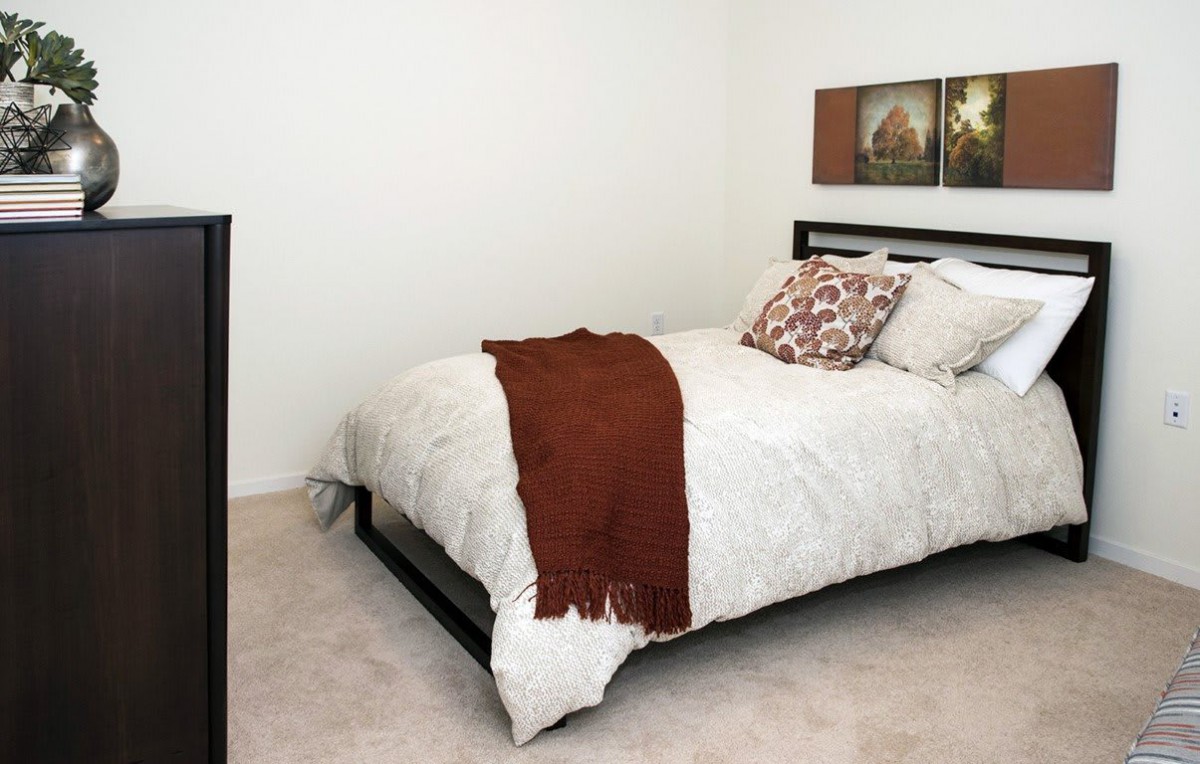 A minimalist bedroom setup with a neatly made bed featuring pillows and a throw blanket.
