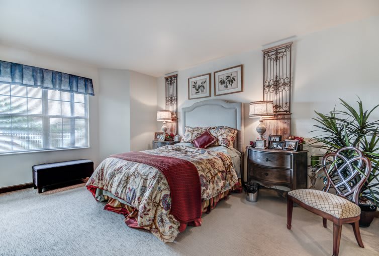 A cozy, traditionally decorated bedroom featuring a bed with a floral comforter, nightstands with lamps, and artwork above the headboard.