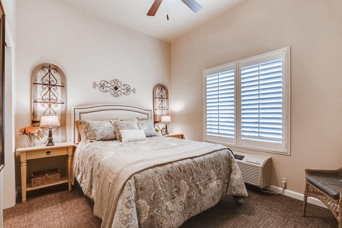 A cozy bedroom with elegant decor, featuring a comfortable bed, stylish lamps, and window shutters.