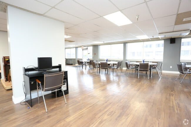 A spacious office area with desks and chairs, featuring large windows and bright lighting.