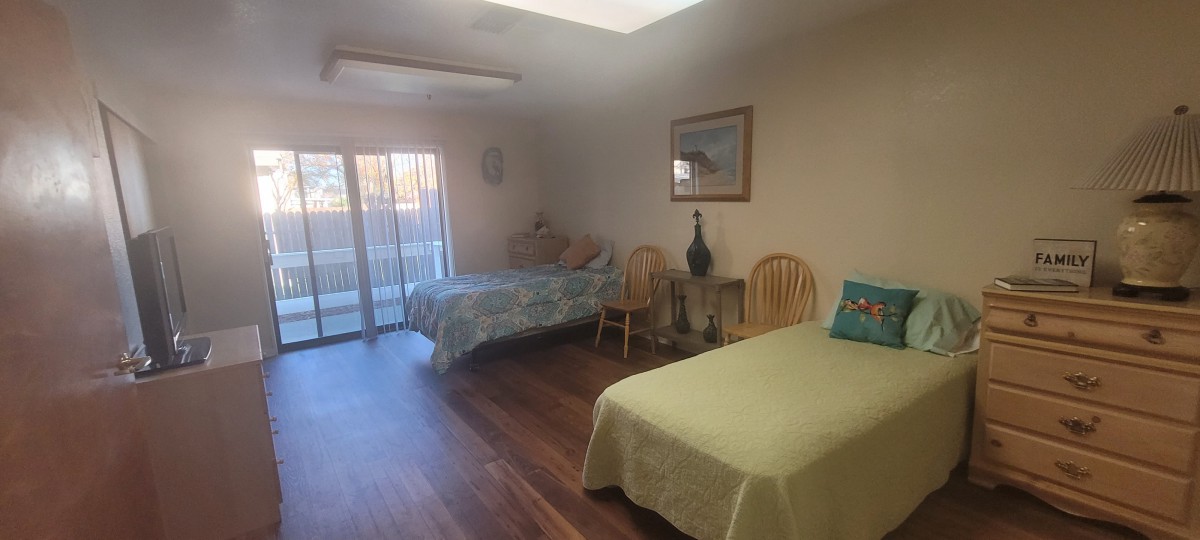 A cozy bedroom featuring two beds, wooden flooring, and ample natural light from a sliding glass door.