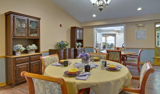 A well-decorated dining room with a round table set for a meal, featuring elegant chairs and a chandelier.