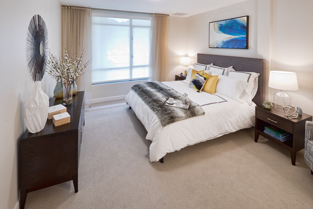A modern bedroom with a large bed, decorated with neutral tones and vibrant artwork on the wall.