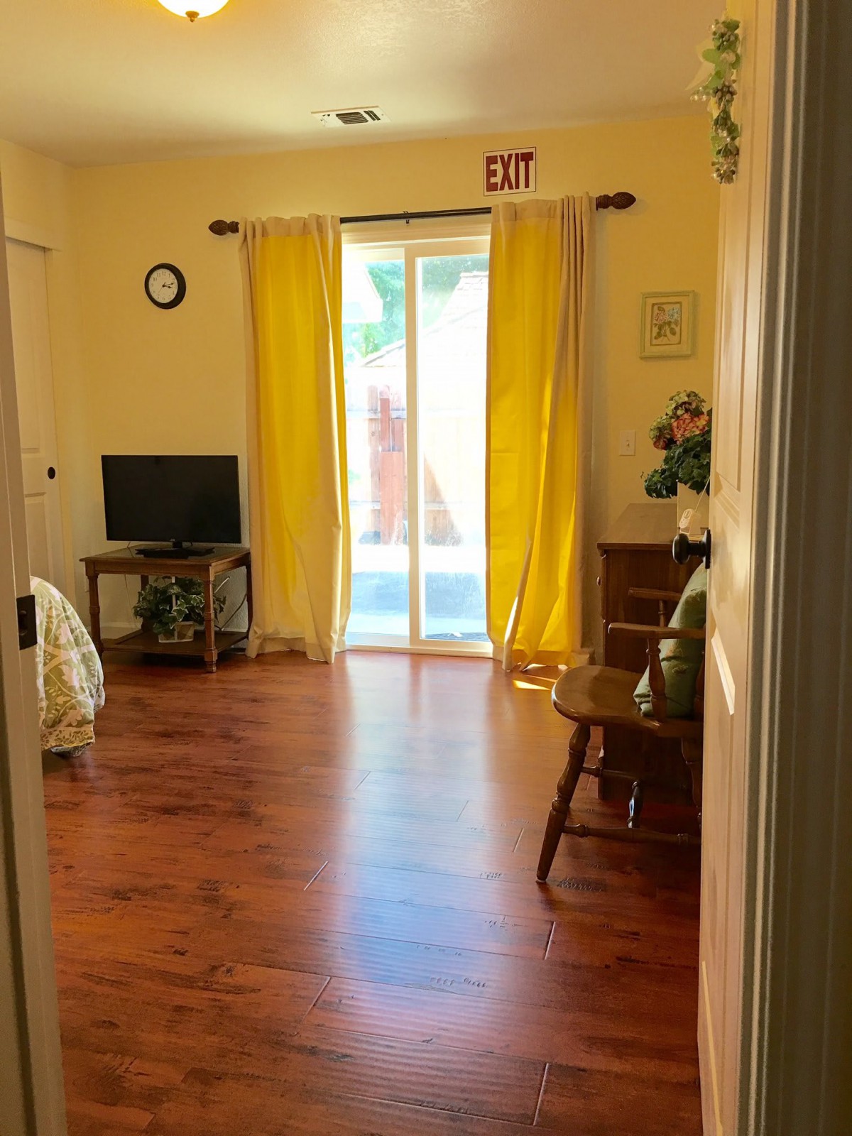 A cozy living room with hardwood floors and yellow curtains letting in the sunlight.