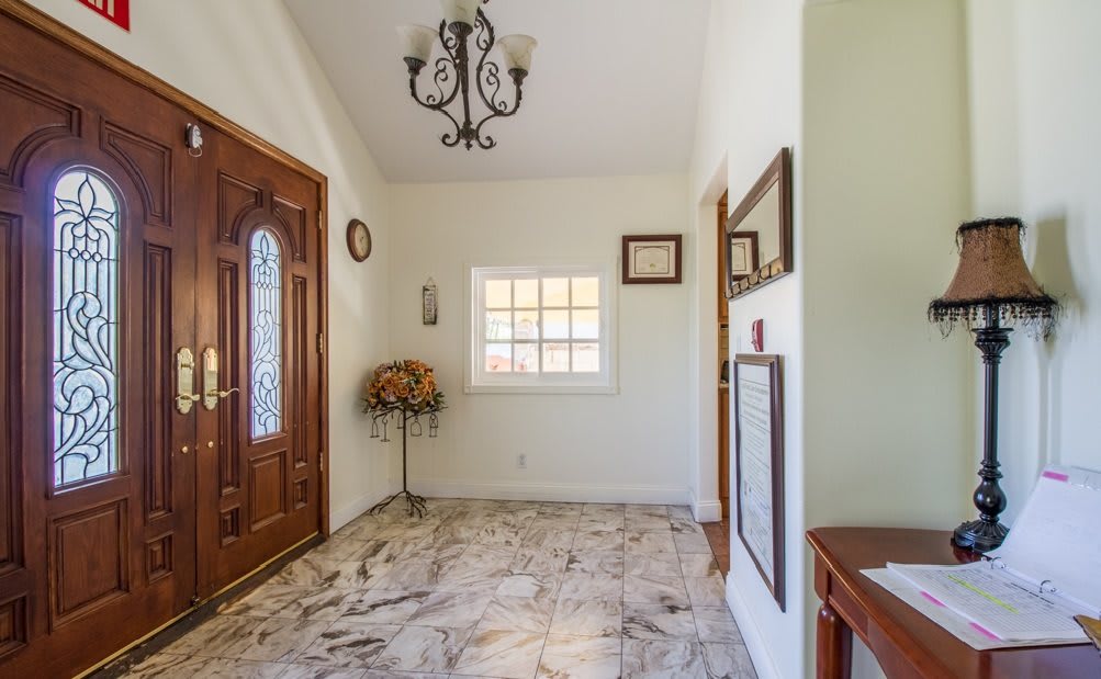 A well-lit entryway featuring a wooden door, decorative chandelier, and tiled floor.