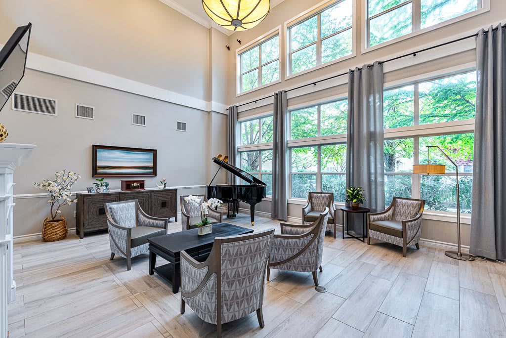 A modern living room featuring a grand piano, large windows, and elegant seating.