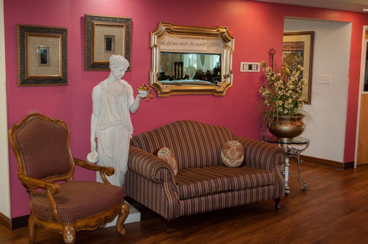 A stylish living room featuring a striped sofa, a classical statue, and decorative mirrors and artwork on a pink wall.