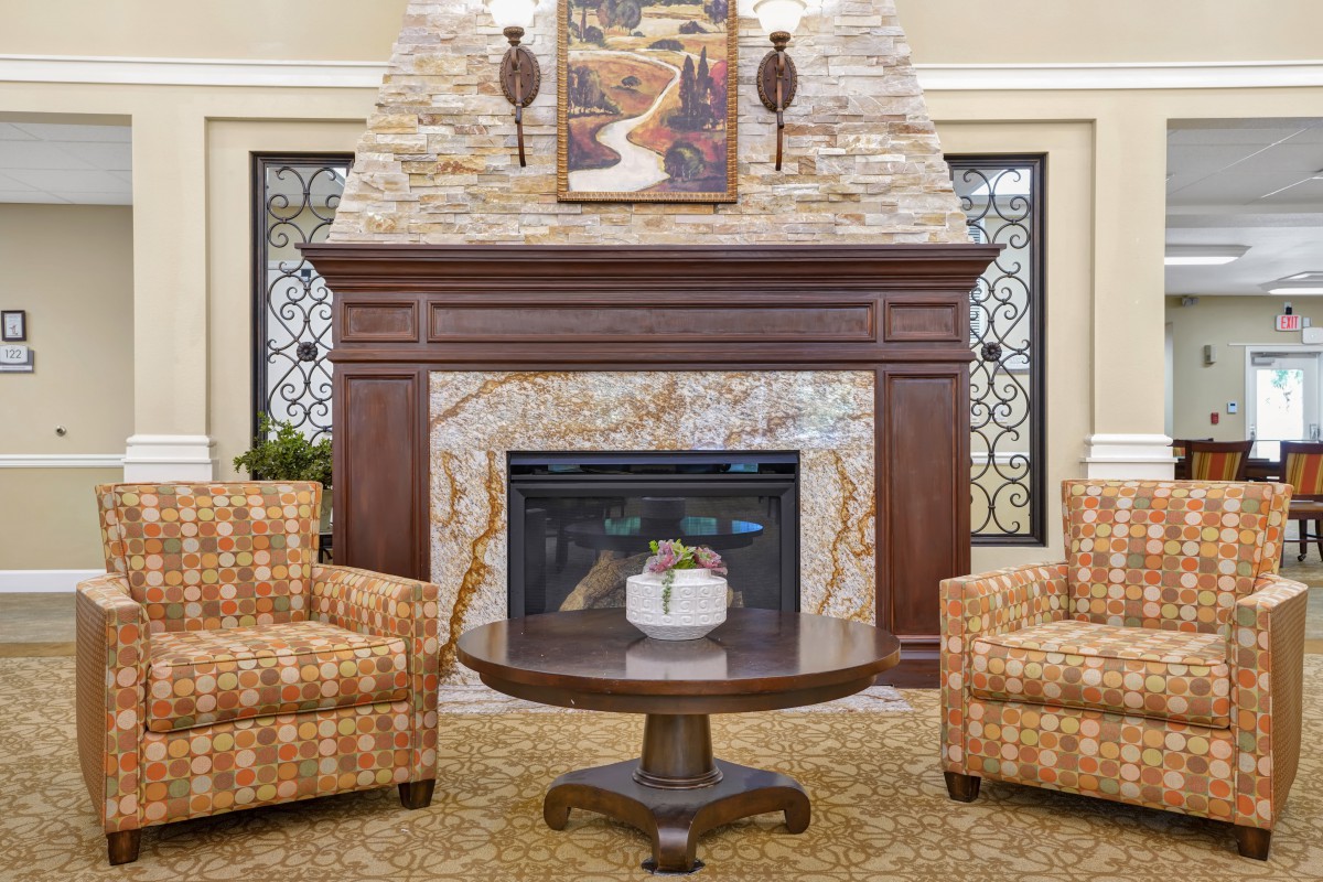 A cozy living room with a stone fireplace, flanked by two patterned armchairs and a round wooden coffee table.