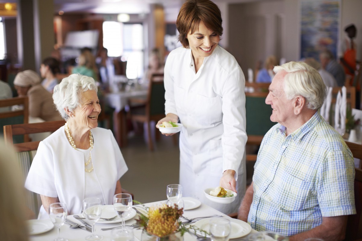 A waitress serves food to an elderly couple at a restaurant.
