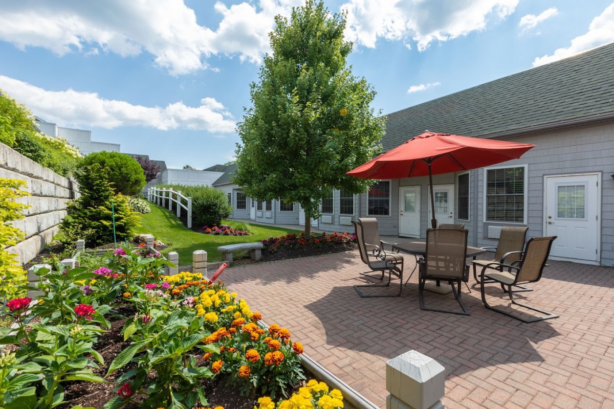 A charming garden patio with colorful flowers, outdoor seating, and a red umbrella on a sunny day.