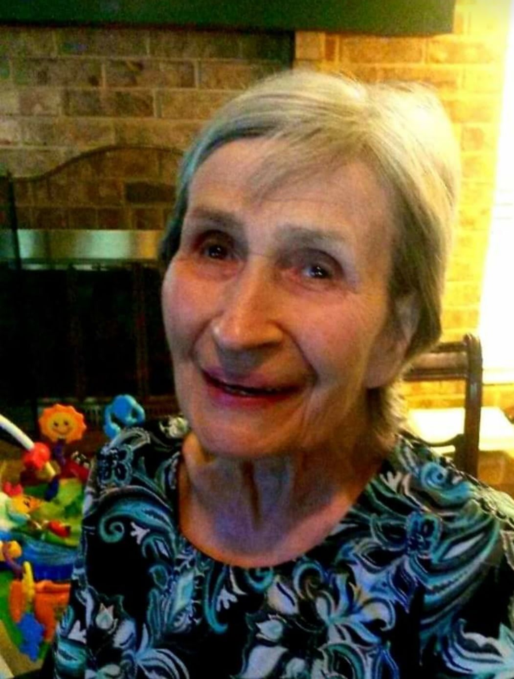 An elderly woman smiles warmly while indoors in casual attire.