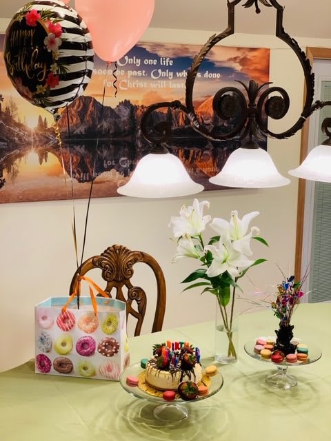 A dining room table set with gift bags, balloons, and flowers for a birthday celebration.