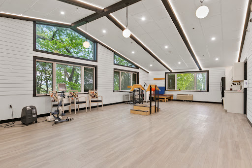 A bright and spacious fitness studio with large windows, wooden floors, and modern decor.