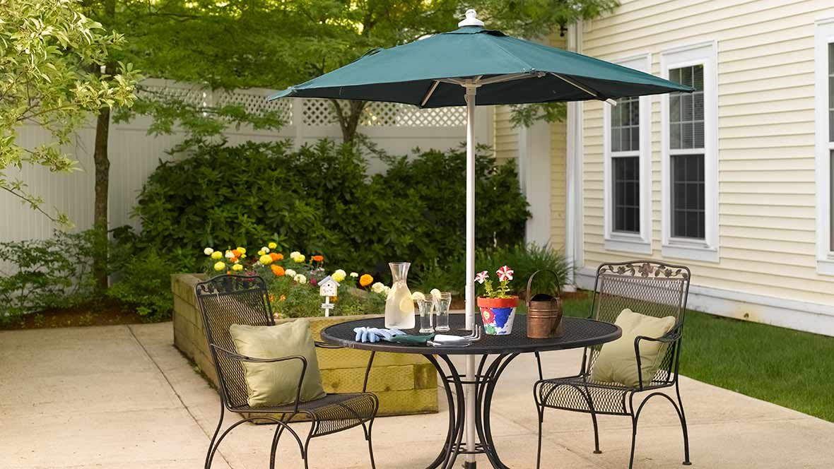 A cozy patio setup with a table, chairs, and an umbrella surrounded by blooming flowers.