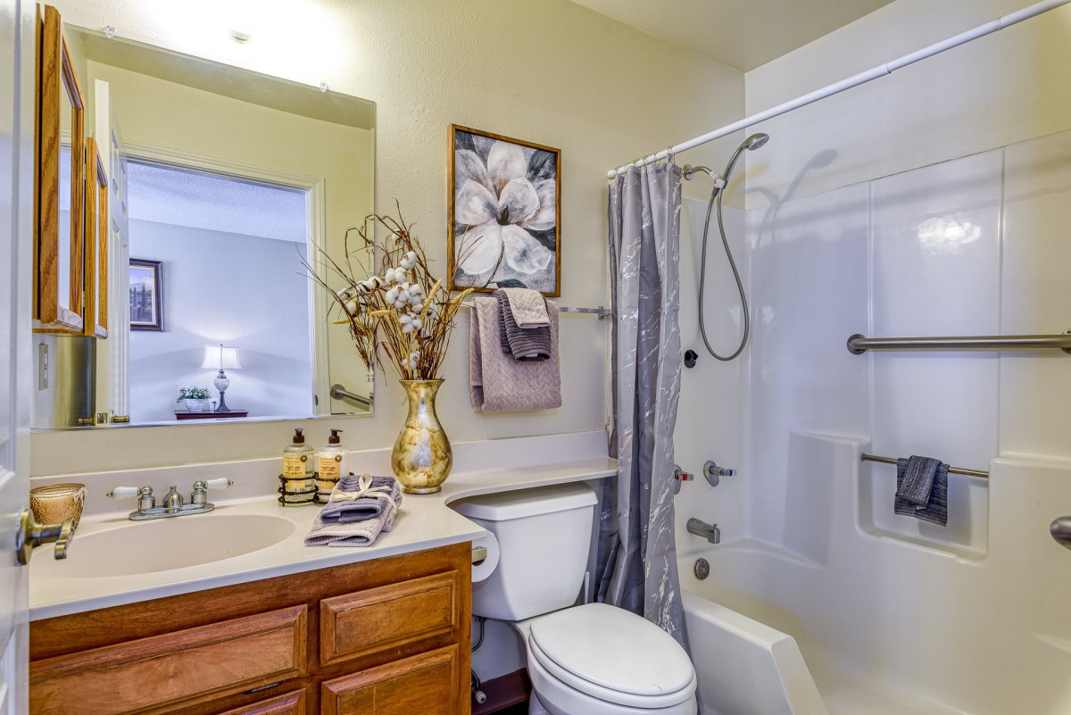 A neatly decorated bathroom with a shower, sink, and wooden cabinets.