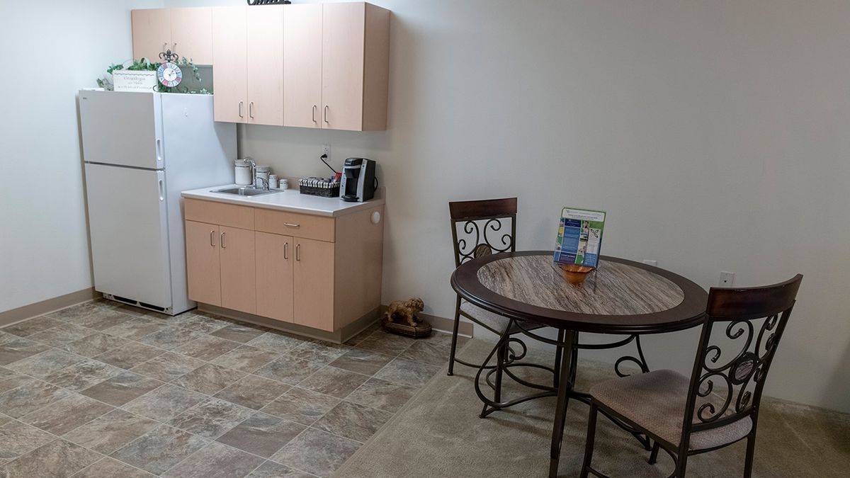 A small kitchenette with cabinets, a coffee maker, and a table with chairs.