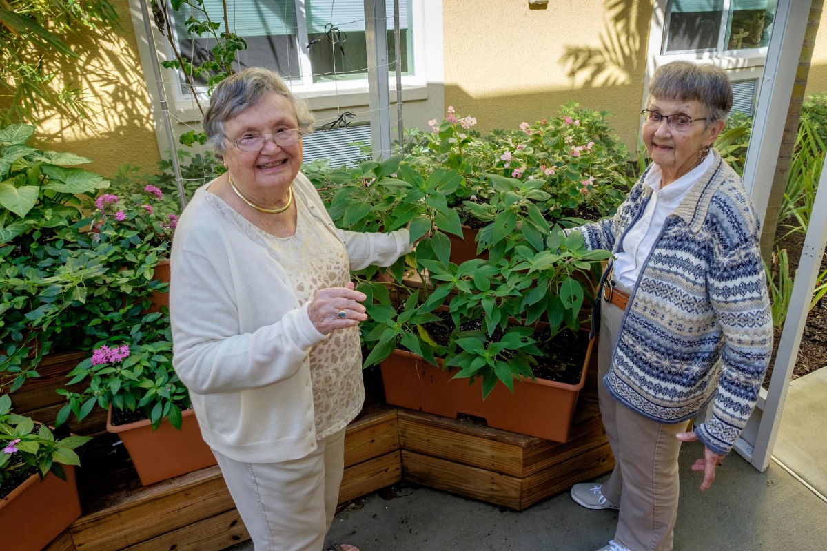 Two elderly women smiling while tending to their garden.