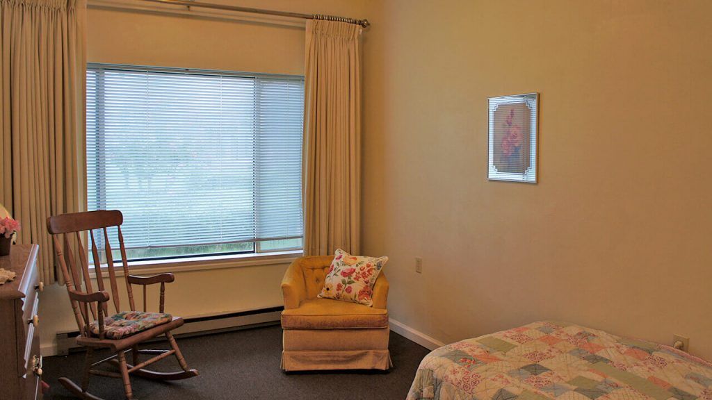 A cozy room with a large window, featuring a comfortable chair, curtains, and a bed.