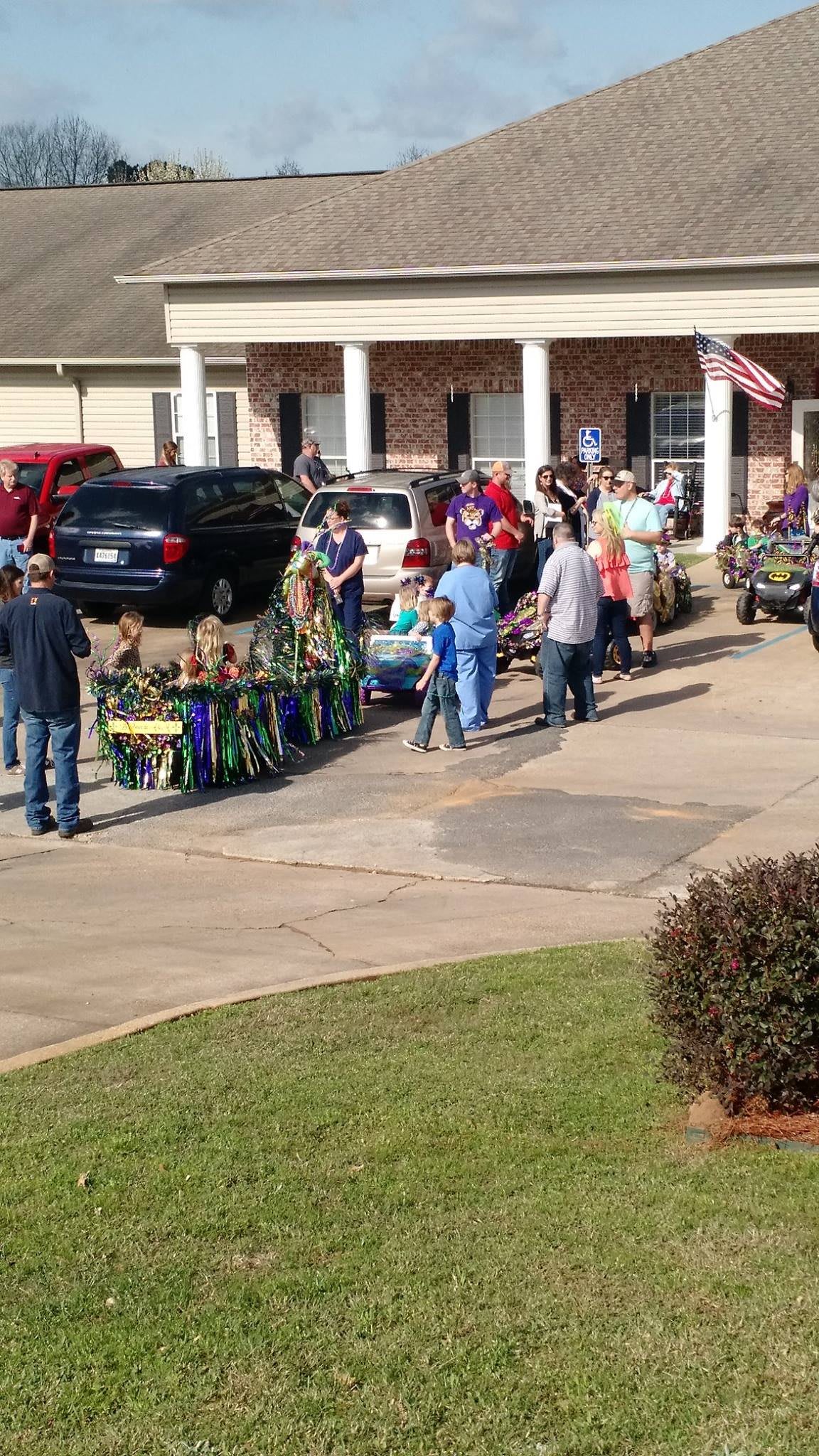 A group of people, including children and adults, participates in an outdoor parade with flags and vehicles.
