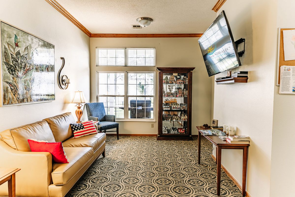 A cozy living room with a sofa, armchair, and TV, featuring decorative elements and ample natural light from a large window.